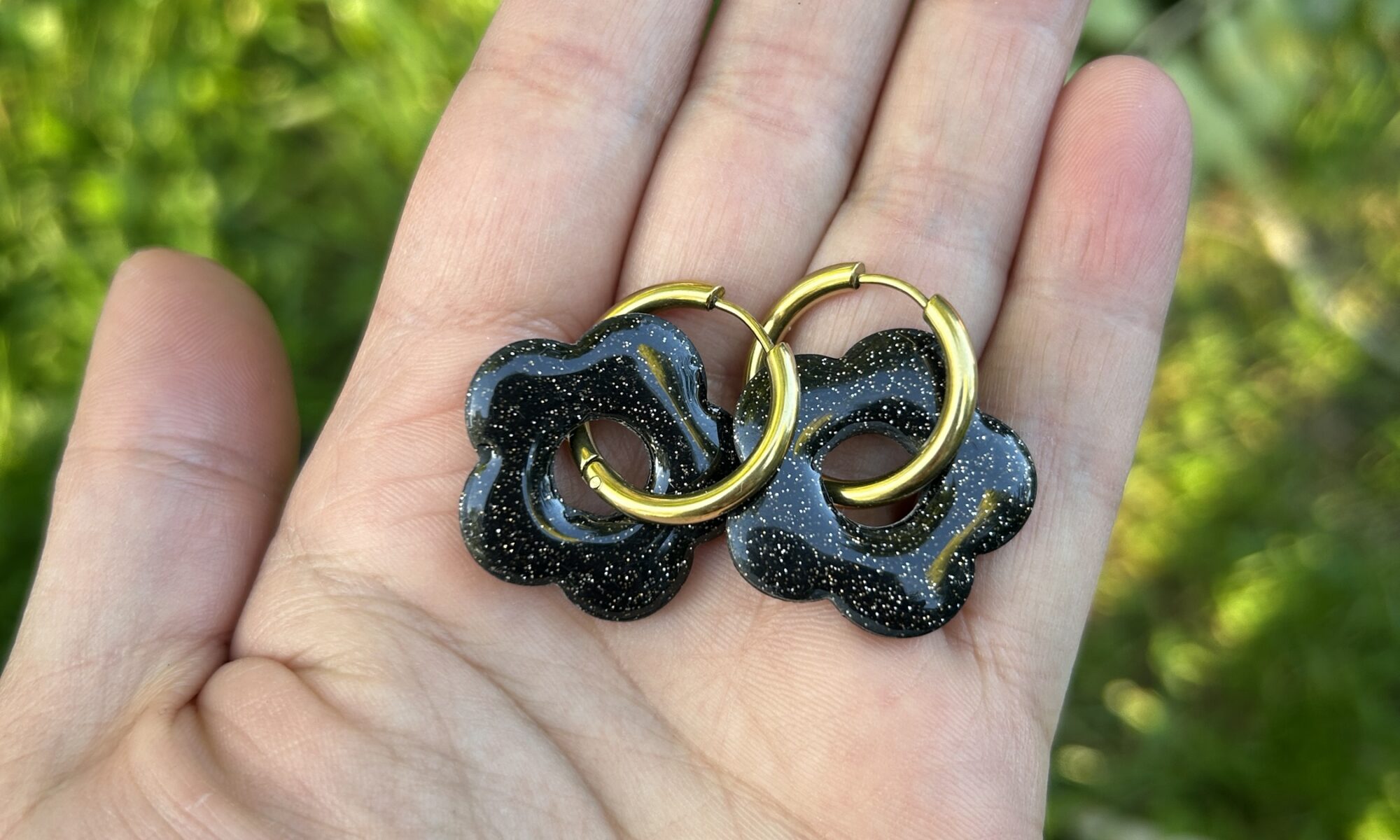 présentation dans une main, paire de buocles d'oreilles, créoles avec pampilles noires et paillettes dorées