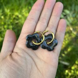 présentation dans une main, paire de buocles d'oreilles, créoles avec pampilles noires et paillettes dorées