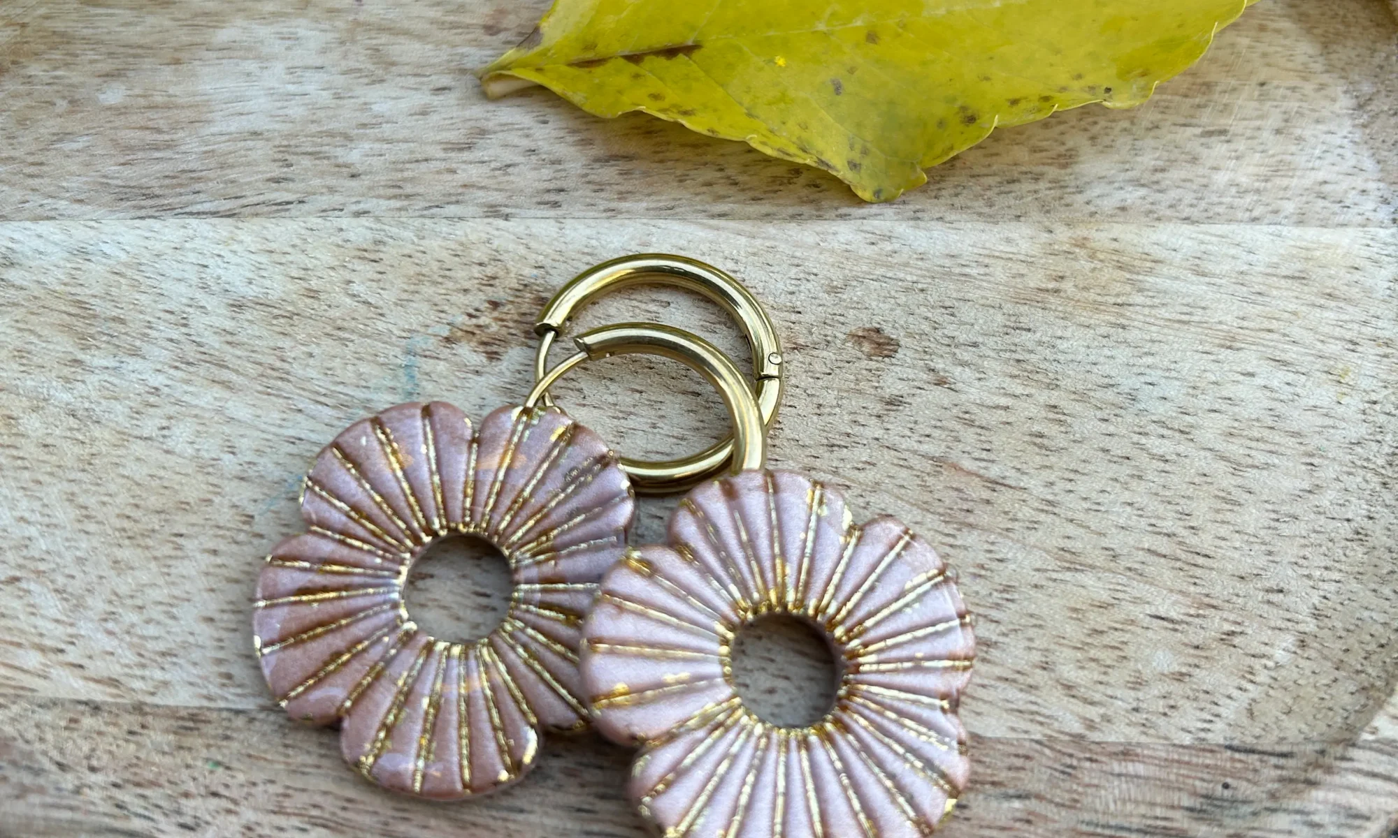 présentation de bijou sur un plateau avec une décoration feuille. Pampilles pour créoles, forme coquelicot, beige et doré