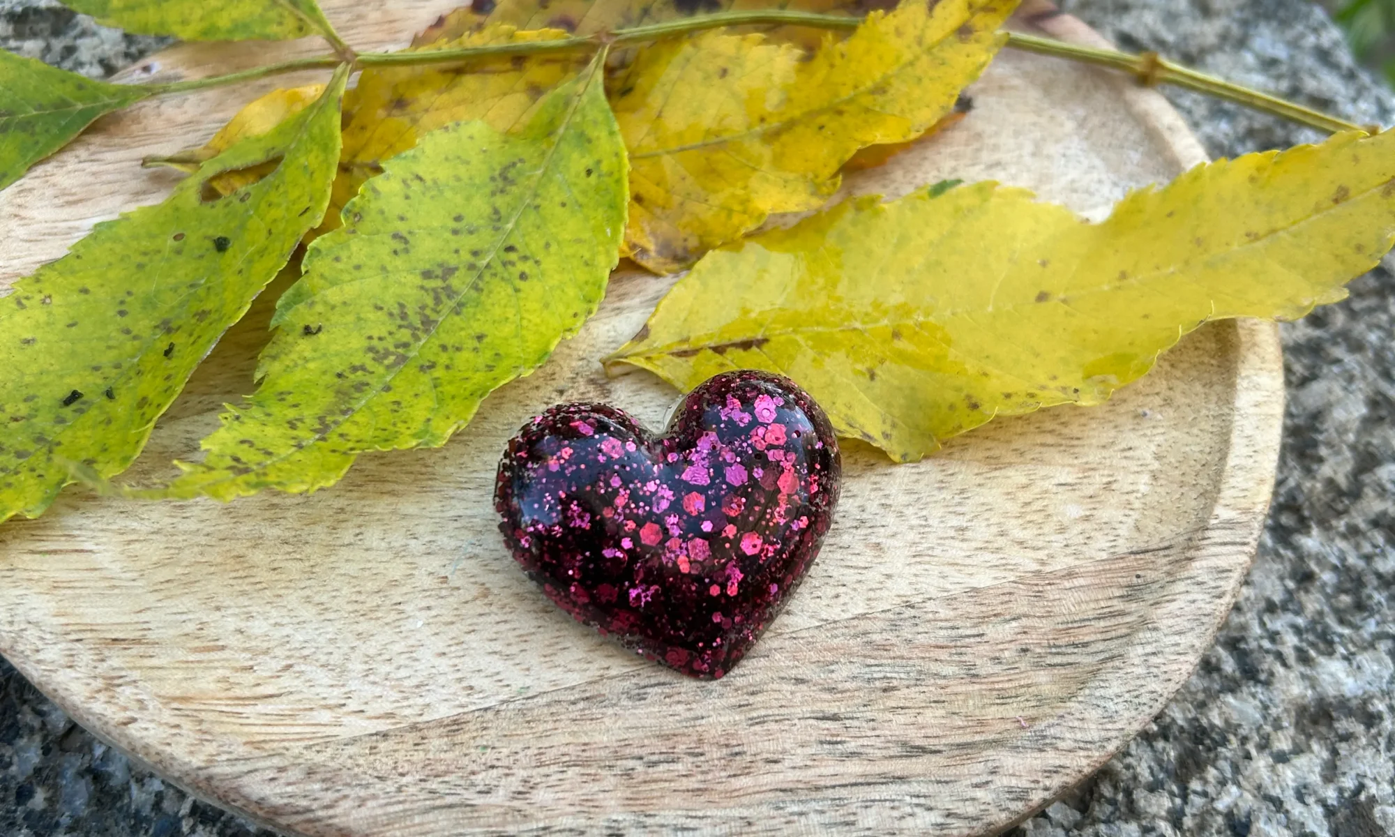 broche en forme de coeur en résine de couleur rose poudré sur un plateau avec déco de feuille