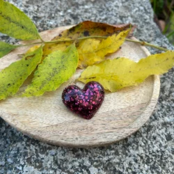 broche en forme de coeur en résine de couleur rose poudré sur un plateau avec déco de feuille